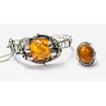 A silver and amber set comprising a bangle set with an oval amber with floral detailing, hinged,