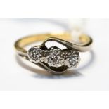 A three stone diamond ring, with cross over detail in 18ct yelow and white gold, finger size K½,