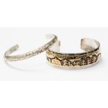 A silver and gold inlaid torque bangle depicting a scene, approx width 18mm,