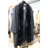 A black wool coat in boucle with a black fur collar and a badge on the coat which says 'Sir Stans