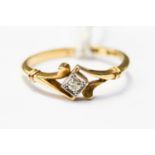 A diamond ring, with scroll shoulders, the diamond set in a square white metal setting,