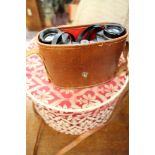 A fabric covered hat box in cream and red with padded lid and a pair of cased Binoculars.