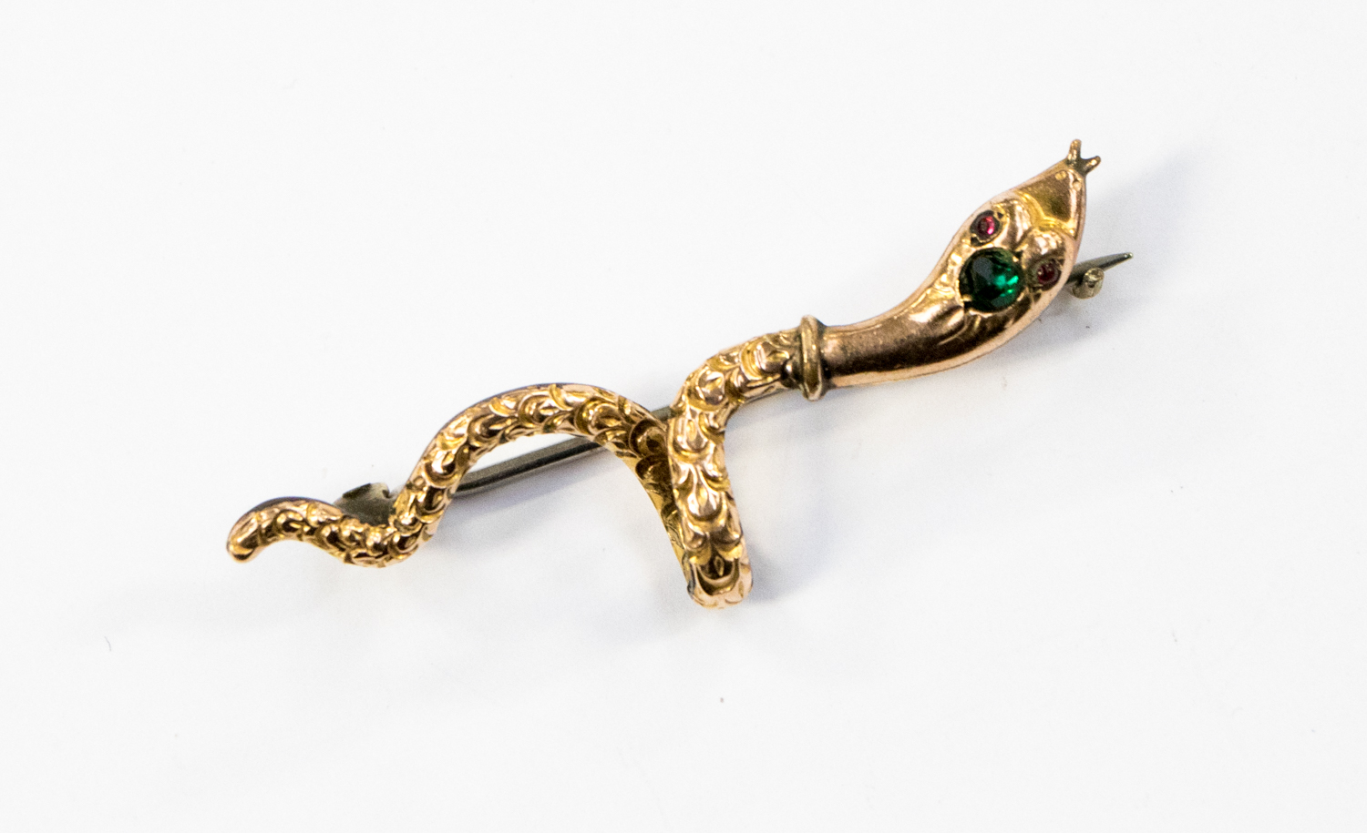 A Victorian serpent brooch in gilt metal, with a green stone set to the head and red eyes,