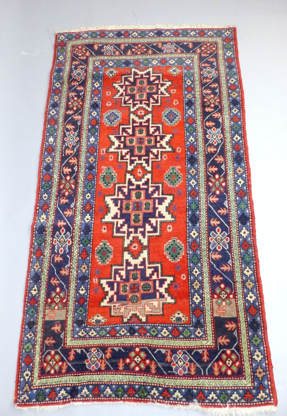 Kazak brick red ground rug, four central star medallions within a wide floral and geometric border,