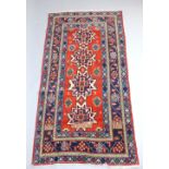 Kazak brick red ground rug, four central star medallions within a wide floral and geometric border,