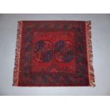 A small Afghan tribal rug with two elephant foot guls on a tomato red field enclosed by running and