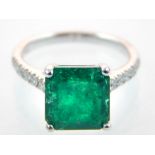Art Deco style 18ct white gold emerald ring, the square cut stone 3.12ct flanked by a 0.