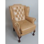 Tan leather wingback armchair, brass effect stud, button back, stub claw & ball feet.