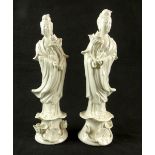 Mirrored pair of blanc de chine figures of guanyin, each holding a flower and raised on a leaf base,