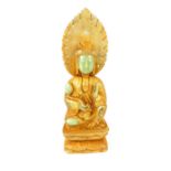 A gilded jade carving of Buddha, hand raised holding a lotus flower, seated on a pedestal, 29.5cm h