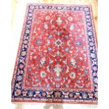 A red ground Indian woollen red ground carpet embroided with stylised flowers within a blue frieze