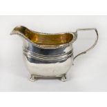 A George III silver cream jug with gilt washed interior, fluted edge, reeded body, on four ball feet