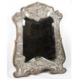 A shaped bevelled mirror in a silver frame with flower and leaf scroll decoration, outset