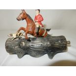 A painted metal table cigarette lighter in the form of a huntsman on horseback jumping a tree trunk