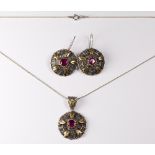 A circular silver pendant mounted with gold coloured metal harebells with centre red stone, on a