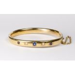 A heavy 18ct. gold stiff hinged bangle set to the top with alternate sapphires and diamonds