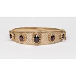 A 9ct. gold stiff hinged bangle set to the top with five garnets