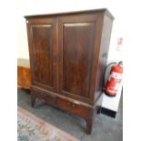 An antique mahogany cupboard on stand fitted two panelled doors, end carrying handles, the base