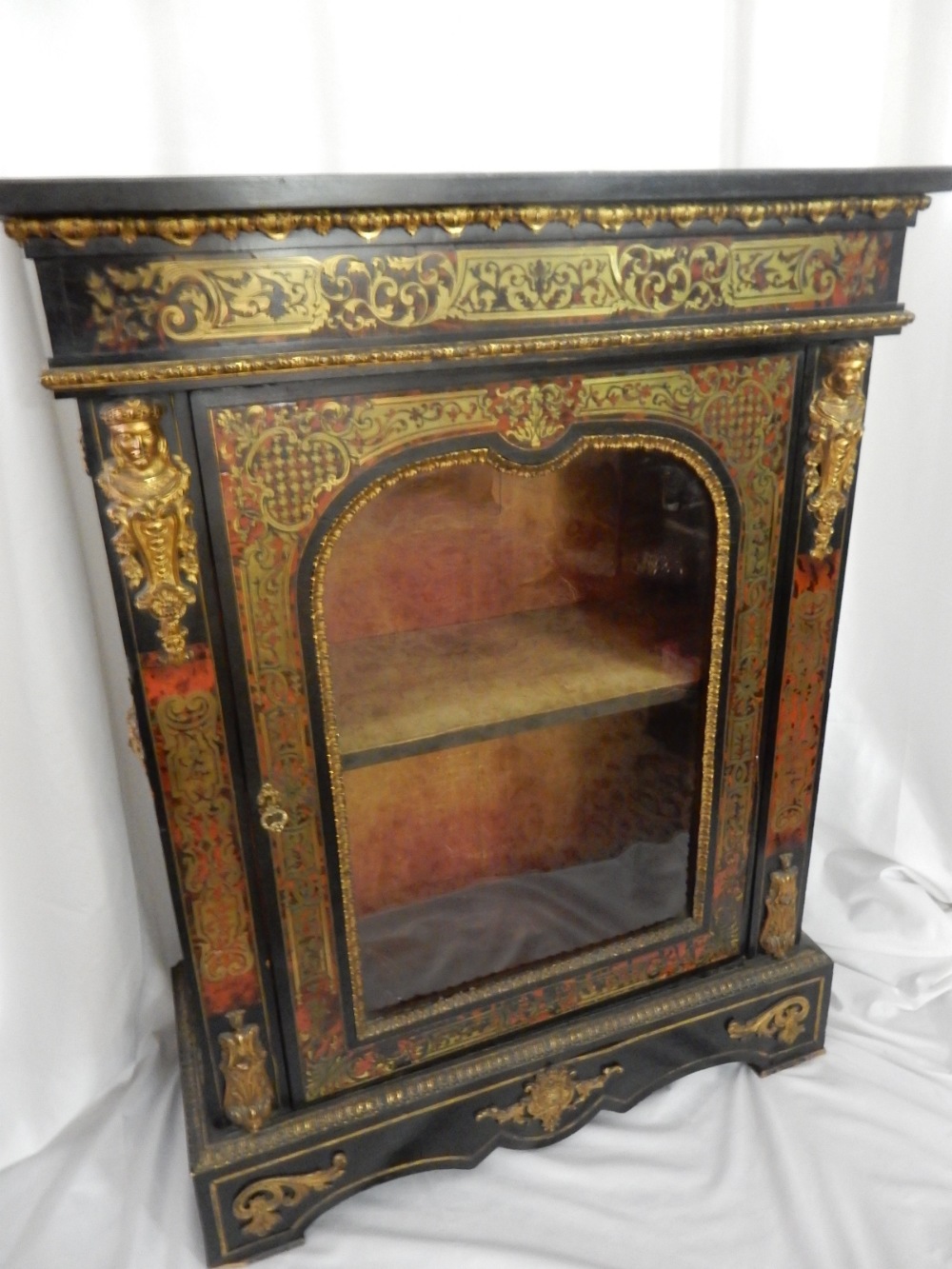 A 19th Century red buhl cabinet with gilded caryatids, shaped glass door enclosing shelves, on