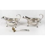 A pair of George III silver sauce boats with serrated edges, leaf clad scroll handles on three pad