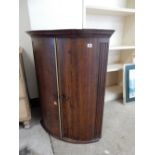 A Georgian oak wall hanging corner cabinet fitted two bow doors enclosing shelves