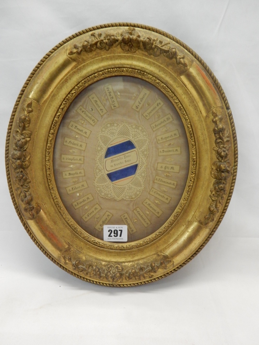 A relique with lace work decoration and Saints names to the border, in an oval gilt frame