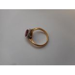 A lady's ring set red stone surrounded by diamonds, on an 18ct. gold shank