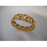 A gold coloured metal hinged bangle with pierced leaf scroll decoration