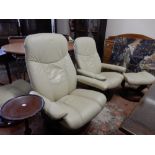 A pair of Stressless revolving armchairs and matching footstools in cream leather