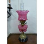 A Victorian brass oil lamp with cranberry glass reservoir and shade