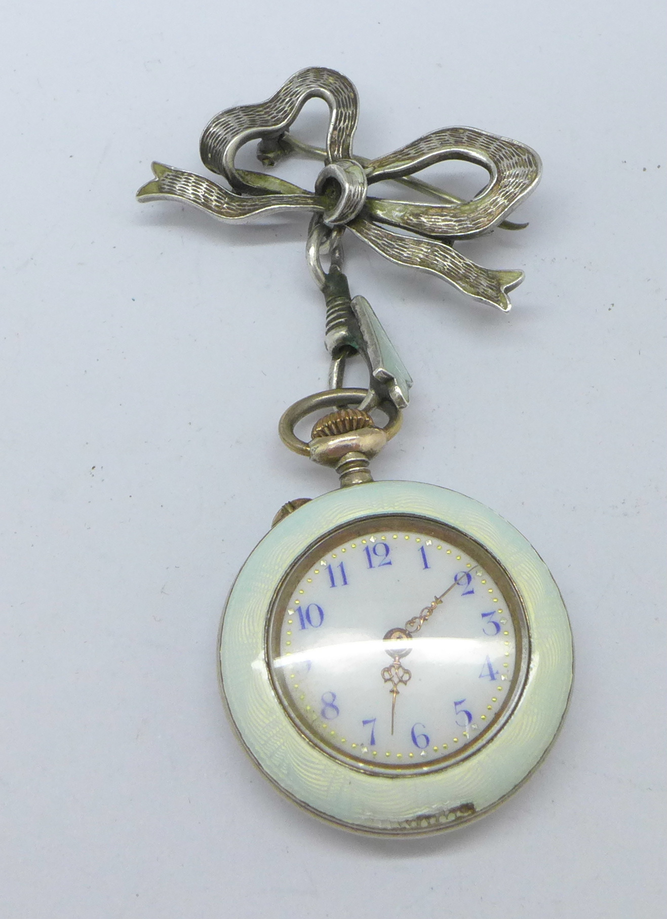A lady's silver and enamel fob watch with decorative case and silver bow brooch,