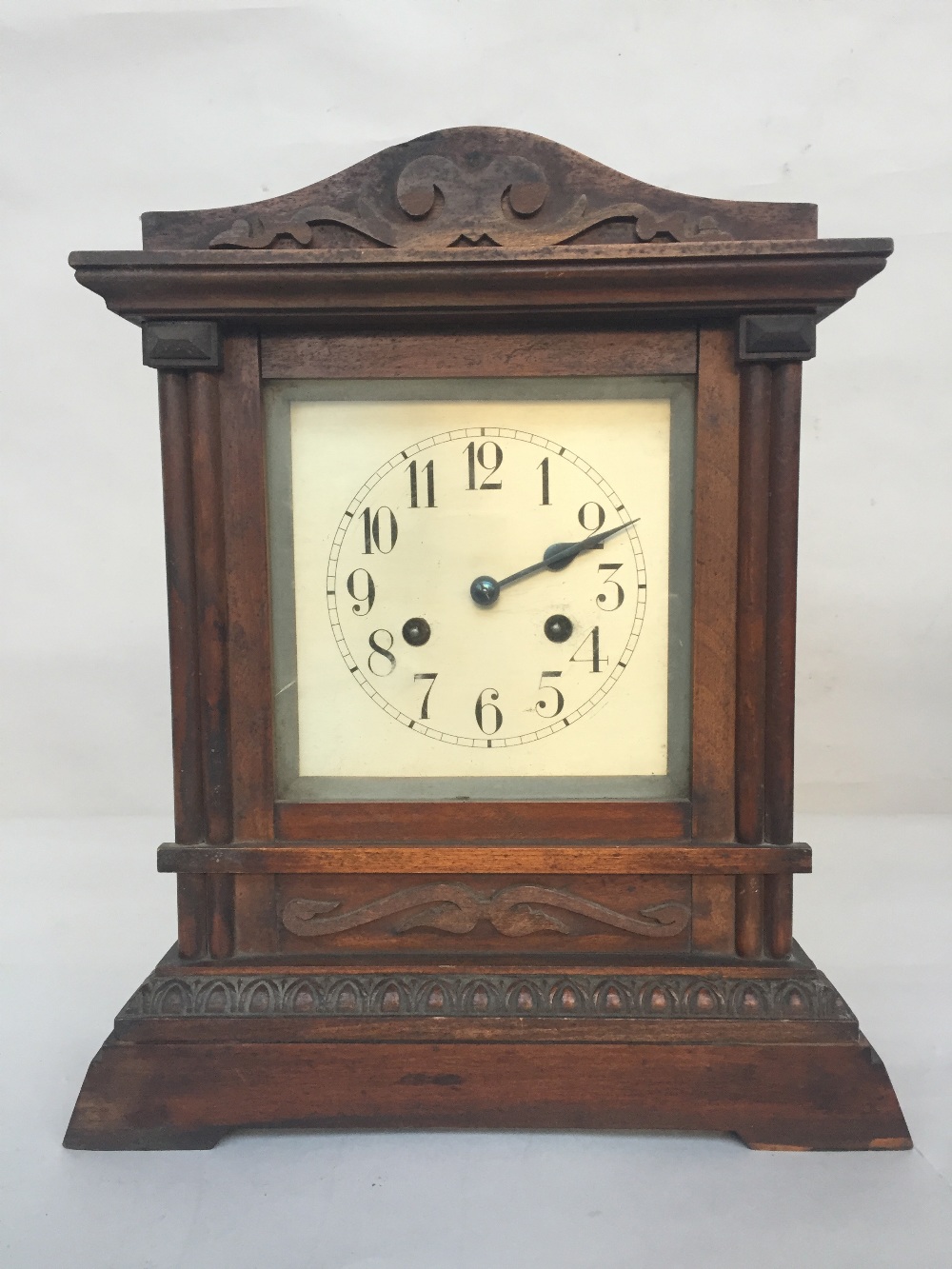 A wooden cased mantel clock with carved pediment,