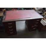 A kneehole desk with an arrangment of eight lockable drawers around a central knee hole with maroon