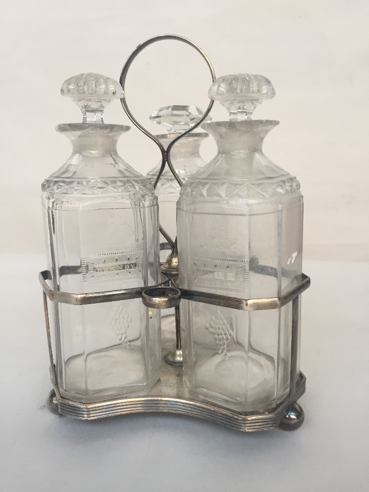 A silver plated three bottle decanter stand on three ball feet with decanters,