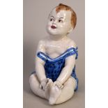 A late 19th century continental faience figurine of a happy baby in a blue dress