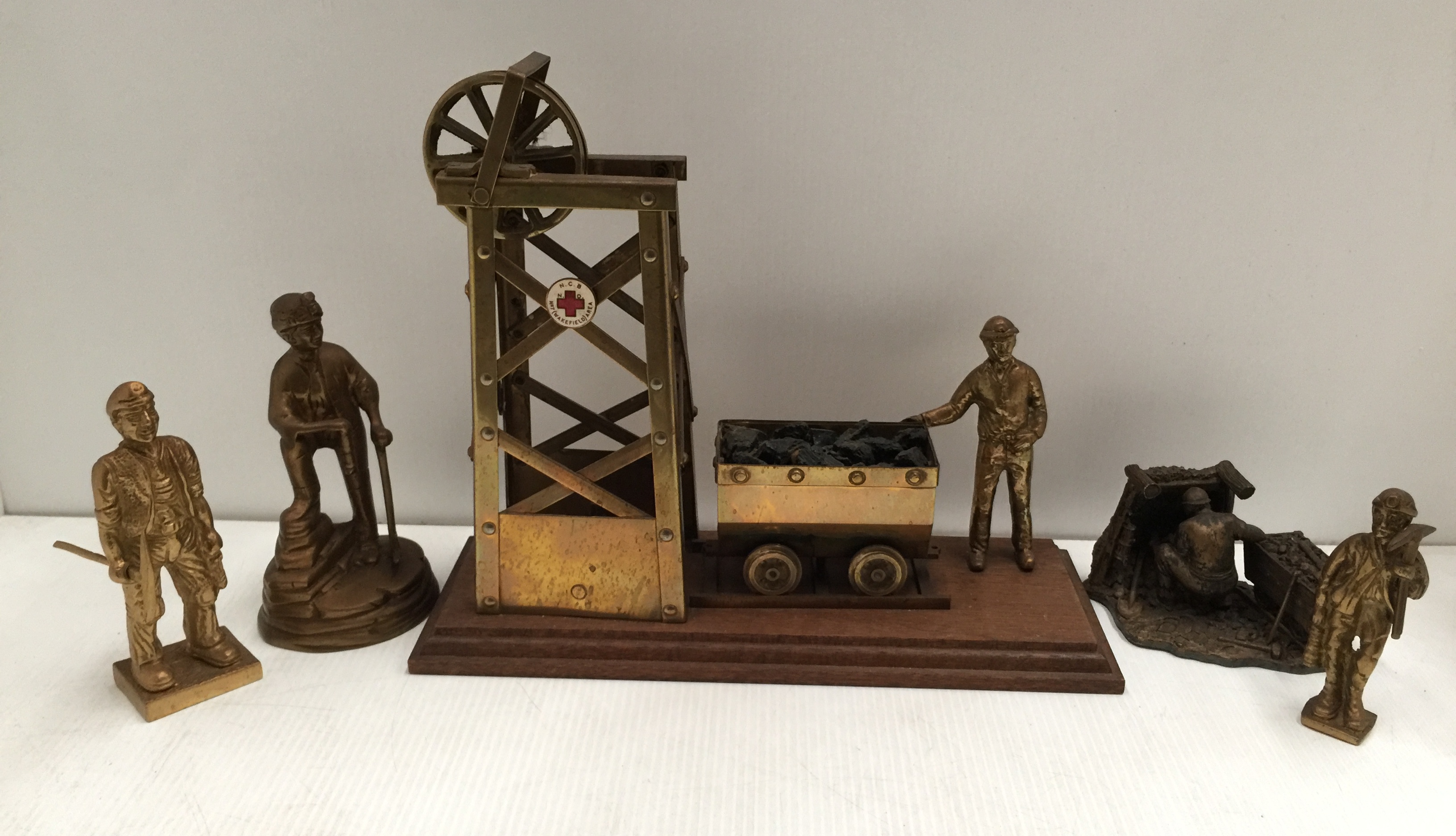 A brass model of a miner with coal bogie and pit head winding gear stamped N.C.