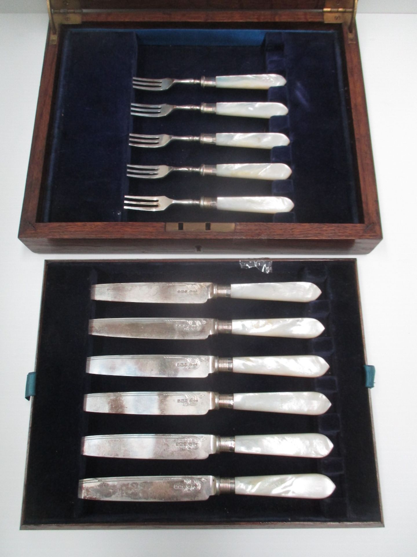 A set of six silver bladed dessert knives with mother of pearl handles and five matching forks [11].