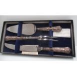 A serving set of carving knife and fork and a cake server with silver cased Kings pattern handles.