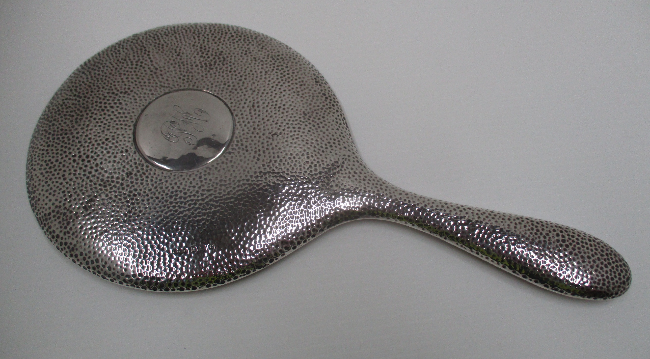 A circular hand mirror with hammered finish, silver back and cased handle.