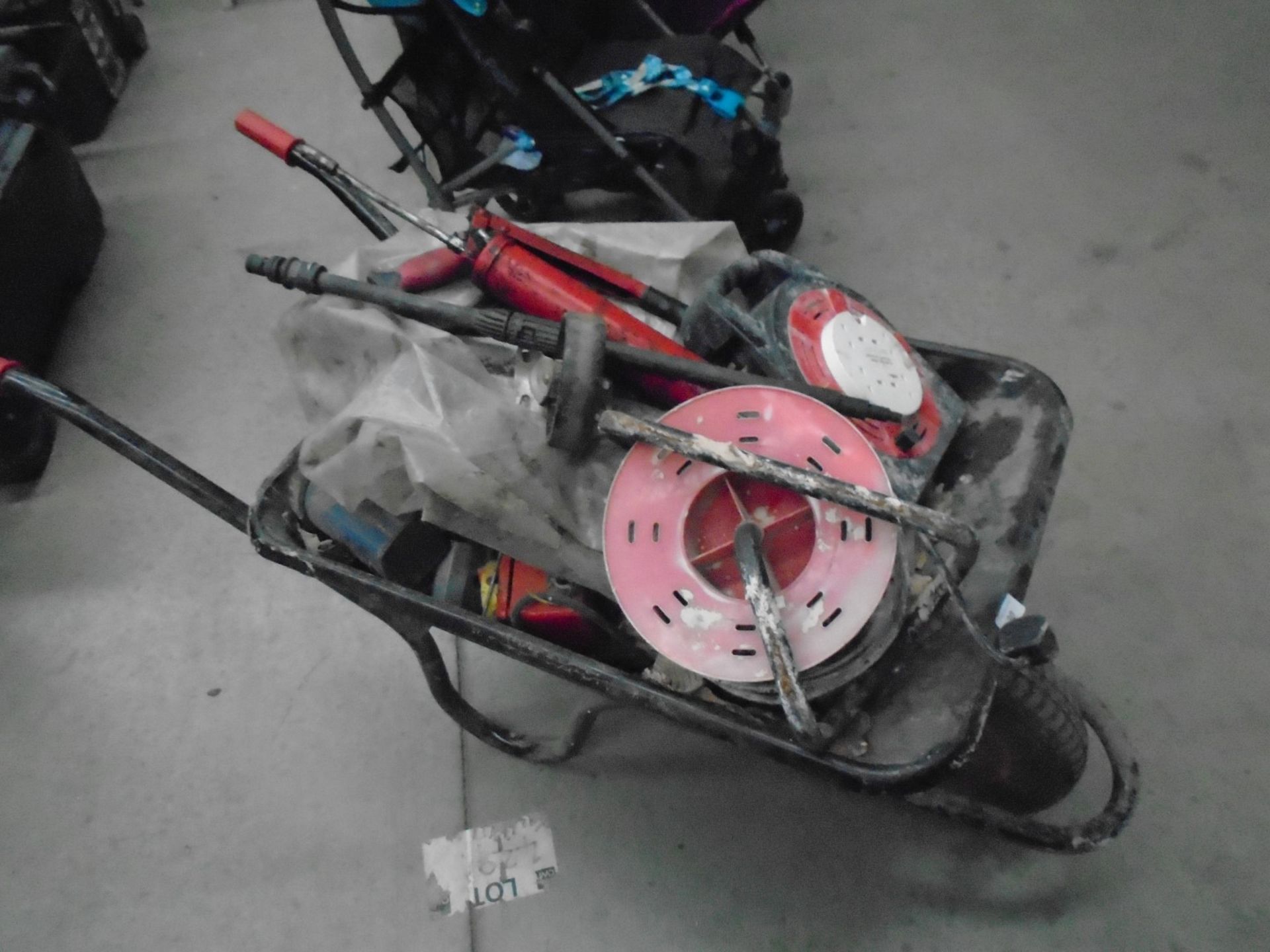 A black metal wheel barrow with contents, 240v extension reels (1 failed earth test), grease guns,