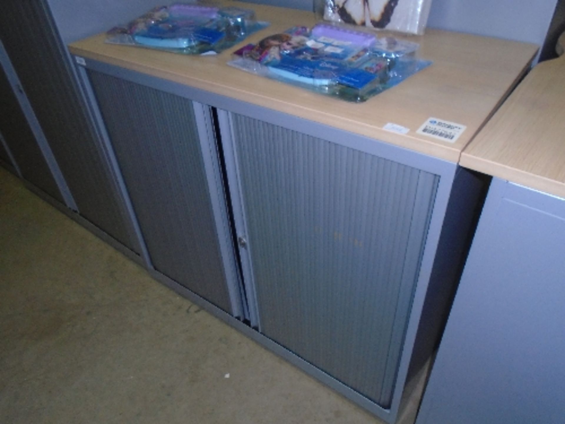 A grey metal framed double sliding tambour front stationery cabinet with light wood top 53 x 100 x