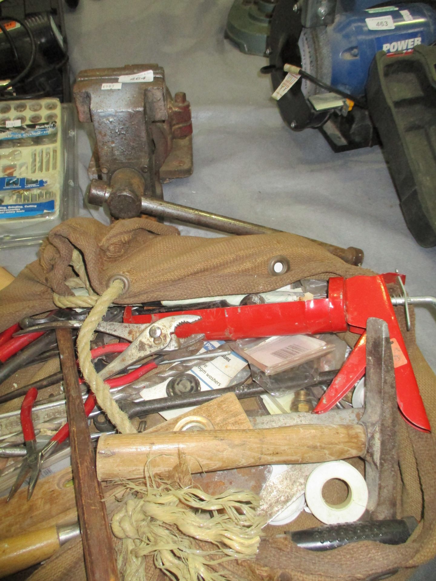 A metal bench vice and a tool bag containing spirit level, slaters/masons hammer, cement trowel,