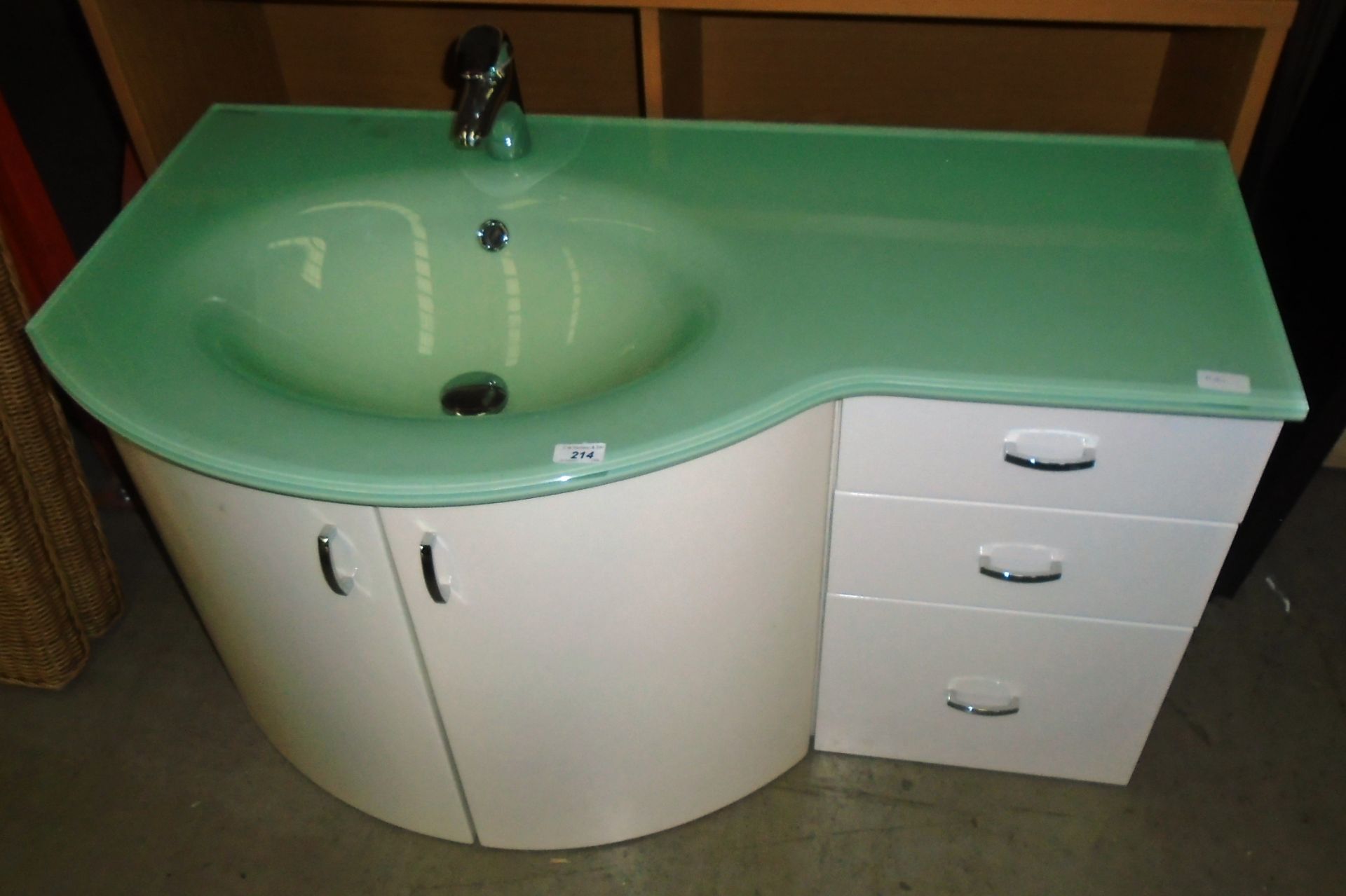 A green frosted wash basin with chrome mixers tap mounted on a white 3 drawer two door cabinet