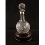 A cut glass round bottom Silver rim decanter on wooden base