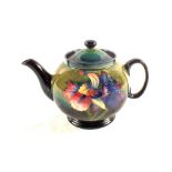 A Moorcroft Orchid pattern teapot on green and dark blue ground,