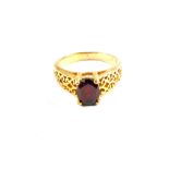 A yellow metal ring with pierced shoulders, set with singe red stone,