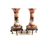 A pair of 19th Century Imari flared neck floral and dragon vases on wooden stands,