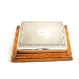 A Silver cigarette box on wooden plinth,