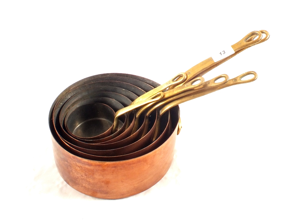 A set of seven graduated copper saucepans with brass handles