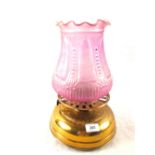 A brass oil lamp with pink glass shade